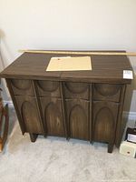 Closed view of vintage sewing cabinet with decorative front panels and a ruler on top for scale.