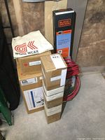Stack of boxes showing Black & Decker hedge trimmer box with cord wrapped around it and multiple other boxes including a garden sprayer box.