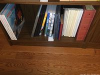 Wood shelf with multiple books and albums containing stamp collections and train books.