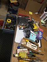 Full view of tools and electrical items spread on table and inside open toolbox drawer including soldering iron in packaging, screwdrivers, testers, wire strippers, measuring tape, and more.