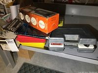 Image of nut driver sets stacked along with other boxes on a table, includes gray cases and various boxes.