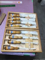 Open wooden two-tier case with eight chisels partially wrapped