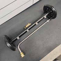 Top view of 15 inch undercarriage power washer attachment showing black coated steel bar with five spray nozzles and two black polymer wheels.