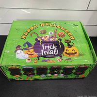 Closed carton box with Halloween artwork showing a purple cauldron filled with candy and decorations, labeled 'Happy Halloween' and 'Trick or Treat!'