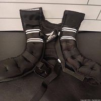 Front view of black weighted vest showing padded compartments and adjustable straps with Zeus logo