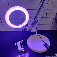 Magnifying lamp illuminated with purple LED light, showing the lamp in working condition with the lamp base and clamp.