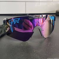 Front view of Pit Viper polarized sunglasses with purple mirrored shield lens and blue Pit Viper logos.