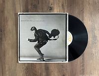 Vinyl LP record with original sleeve featuring Bryan Adams mid-stride holding a guitar, placed on wooden surface.