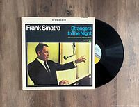 Photo showing Frank Sinatra 'Strangers In The Night' vinyl LP partially pulled out of the cover, cover shows minor wear consistent with VG+ condition, vinyl appears in good condition with no visible major scratches.