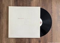 Black vinyl record partially pulled out from white sleeve on wooden floor