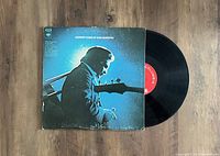 Vinyl LP record partially out of its album cover placed on wooden surface. Sleeve features blue-toned photo of Johnny Cash singing and playing guitar at microphone, album title at the top.