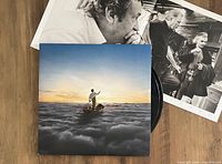 Vinyl record album cover showing a person rowing a boat through clouds at sunset along with black and white booklet photos of band members partially visible in background
