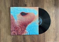 Black vinyl LP record partly inside the album cover which shows Pink Floyd's Meddle album artwork of a human ear underwater with ripples in blue water.