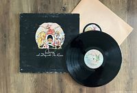 Photo shows the Queen 'A Day At The Races' vinyl LP, its outer sleeve with artwork, and plain cream inner protective cover laid on a wooden surface.