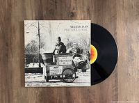 Black vinyl record with a black and white sleeve showing a man with a pretzel cart outdoors. Record partially out of the sleeve showing yellow and red center label.