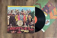 Vinyl LP record and cover of The Beatles Sgt. Pepper's Lonely Hearts Club Band 1974 pressing with original insert showing colorful cover art and vinyl record partially out of sleeve.