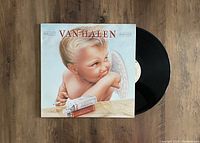 Photo showing the Van Halen 1984 LP vinyl record partially pulled out of its cover, showcasing the iconic album artwork of a cherub with cigarette and pack of cigarettes on a wooden surface.