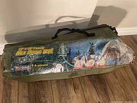 Closed green carry bag with printed label showing Woods 12x10 family hex dome tent, Drytanium branding, and 5-6 person capacity.