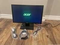 Acer 22 inch LCD monitor powered on showing Acer logo on screen with power and video cables displayed in front.