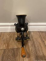 Front view of the antique cast iron coffee grinder showing the opening hopper and wood-handled crank.