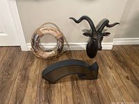 Photo of all three items together: faux ram head, arrow light/sign, and circular buoy on floor.