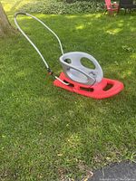 Angle showing red sled with metal handle and gray seat with holes, on grass.