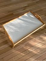 Top view of the wooden bed table tray showing the white flat surface and wooden frame with handles.