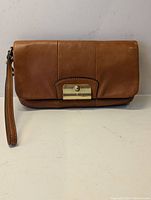 Front view of tan leather Coach Kristin clutch showing gold-tone turn-lock closure and wrist strap.