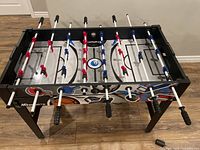Full view of foosball side showing player rods, players in red and blue, handles and black legs of the table.
