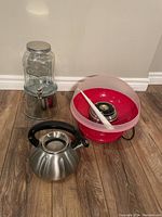 All three items shown on wooden floor: cotton candy maker, glass beverage dispenser, stainless steel kettle.