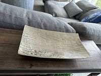 Silver decorative tray on dark wooden surface showing wood grain texture and slightly curved shallow design.