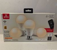 Front view of Globe smart LED lightbulbs box showing 4 bulbs, Wi-Fi indication, warm white 3000K label, app compatibility, and bulb images.