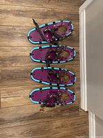 Two pairs of junior snowshoes placed on wood floor, showing full length and strap details.
