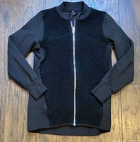 Front view of black women's jacket showing sherpa fleece front panel with contrasting smooth fabric sleeves and full silver zipper closure.
