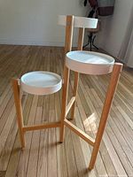 Three-tier indoor plant stand made of light wood with white metal trays for holding plants shown from a side angle on wooden floor.