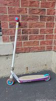 Side view of white and purple Razor scooter with blue wheels, pink handle grips, and folding mechanism at stem.