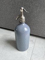 Front angle photo showing the grey vintage Argentinian seltzer syphon bottle with embossed details and metal siphon dispenser.