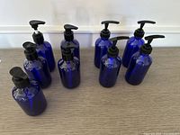 Five round blue plastic bottles with black pumps shown grouped together on a gray surface.