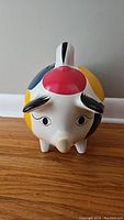 Front view of colorful folk art piggy bank with facial detailing and coin slot on top