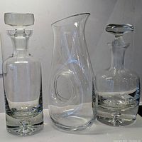 Image of 2 glass decanters with bubble teardrop design and matching stoppers, and glass pitcher/carafe with inlaid handle, all clear glass with heavy bottoms.