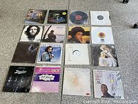 Overhead photo of 16 vinyl record albums arranged on carpet showing front covers and some records removed from sleeves.