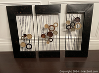Front view of the three-piece brown metal wall art with copper shades in circular patterns suspended by wires in rectangular frames.