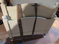 White wooden single bed headboard and footboard held together with straps, showing some wear