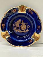 Top-down view of round cobalt blue ashtray with gold decorative motifs showing minor wear.