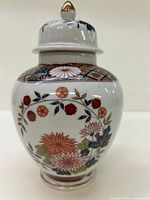 Front view of a white porcelain lidded jar with detailed Asian floral patterns and geometric border design near the top.