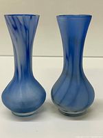 Front view of two blue glass vases showing the swirl pattern and distinct bulbous bases and neck shapes.