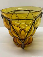 Front angled view of amber glass vase with dark metal frame showing faceted shapes of glass