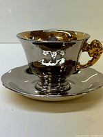Photo of reflective silver teacup on saucer showing side and handle details.