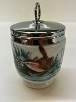 Porcelain sugar bowl with silver lid showing hand-painted bird and natural scenery