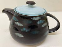 Side view of the Denby Camelot teapot showing black ceramic body with blue leaf pattern and light blue lid with black knob.